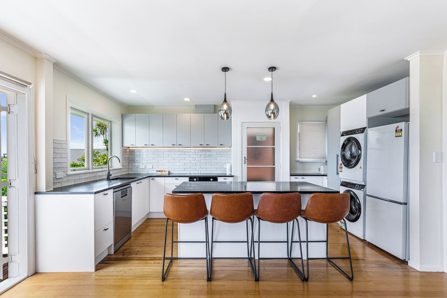 A modern kitchen with a central island, bar stools, a washing machine, and a refrigerator.