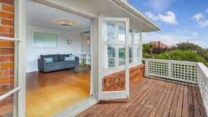 Una terraza de madera con barandilla blanca, un sofá gris y una pared de ladrillo.