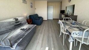 A compact living space with a sofa, a small dining table with chairs, a TV, and a cabinet. - Seafront studio with balcony and parking (Saint-Jean-de-Monts)