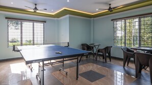 Ein Zimmer mit Tischtennisplatte, Deckenventilatoren und großen Fenstern.