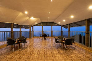 A covered outdoor seating area with wooden flooring and metal railings, featuring tables and chairs. - Avadale Idukki - Stag Groups Not Allowed (Idukki)