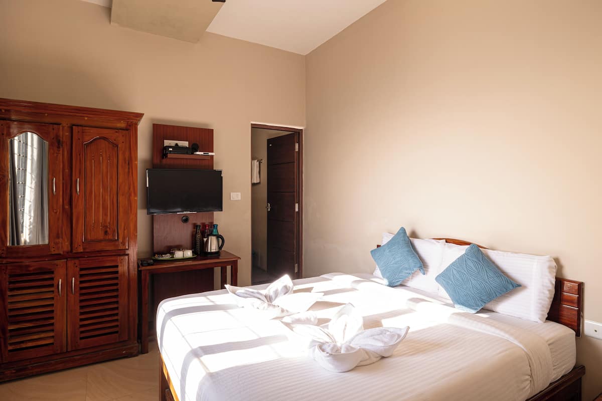 A hotel room with a bed, a wooden wardrobe, a television, and a door leading to another room.
