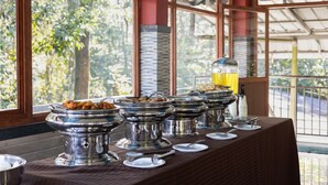 Ein reichhaltiges Buffet mit mehreren Speiseauslagen, einem Kaffeeautomaten und Blick auf Bäume durch große Fenster.
