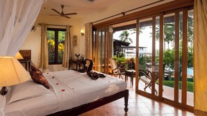 A bedroom with a bed, a ceiling fan, a nightstand, a lamp, and a view of the outdoors. - Anandalakshmi Ayurveda Retreat (Neyyattinkara)