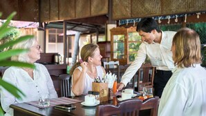 A restaurant with wooden interiors, tables with menus, and a waiter serving food. - Anandalakshmi Ayurveda Retreat (Neyyattinkara)