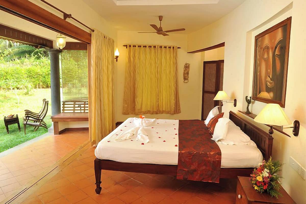 A hotel room with a bed, a nightstand, a lamp, a painting, and a view of a garden.