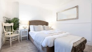 Un dormitorio con una cama grande, una silla blanca, una mesita de noche y un espejo en la pared.