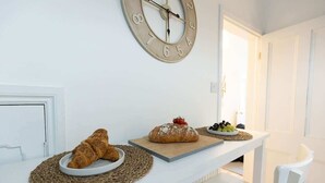 Desayuno con cruasanes y pan sobre una mesa blanca, un reloj en la pared y vista a una puerta.