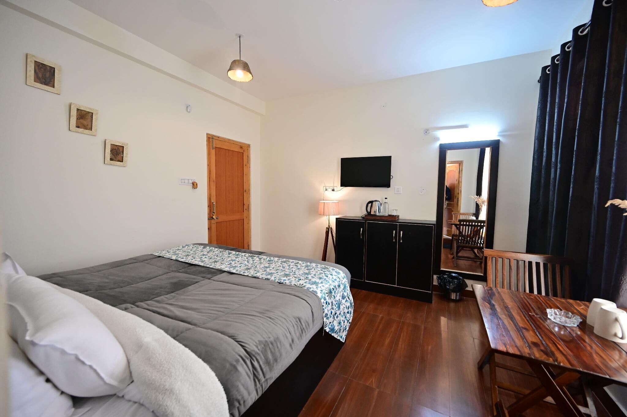 A bedroom with a bed, a desk, a chair, a TV, and a door leading to a dining area.