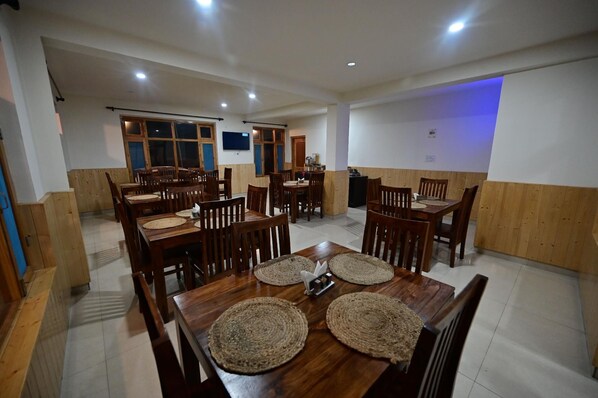 A dining area with multiple wooden tables and chairs, equipped with woven placemats and a central decorative piece. - The Bulevar - Alpine (Lahul)