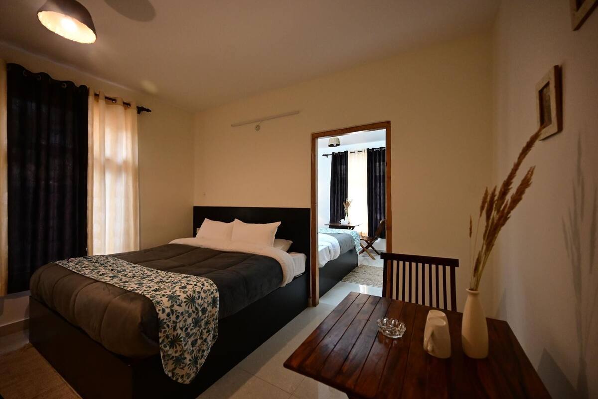 A bedroom with a large bed, a wooden table with a vase, and a view into another room.
