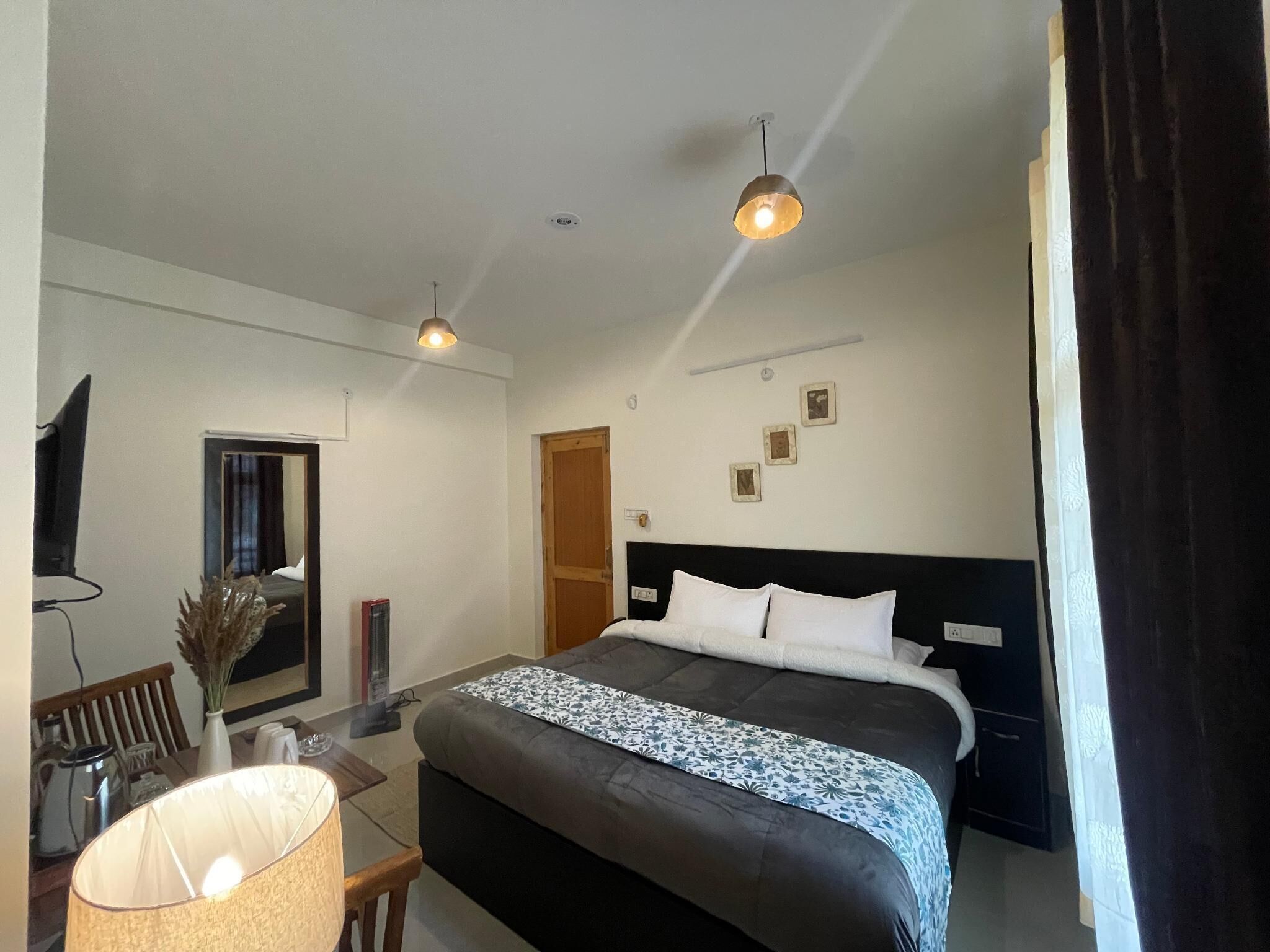 A hotel room with a bed, a desk with a lamp, a chair, a TV, and a door.