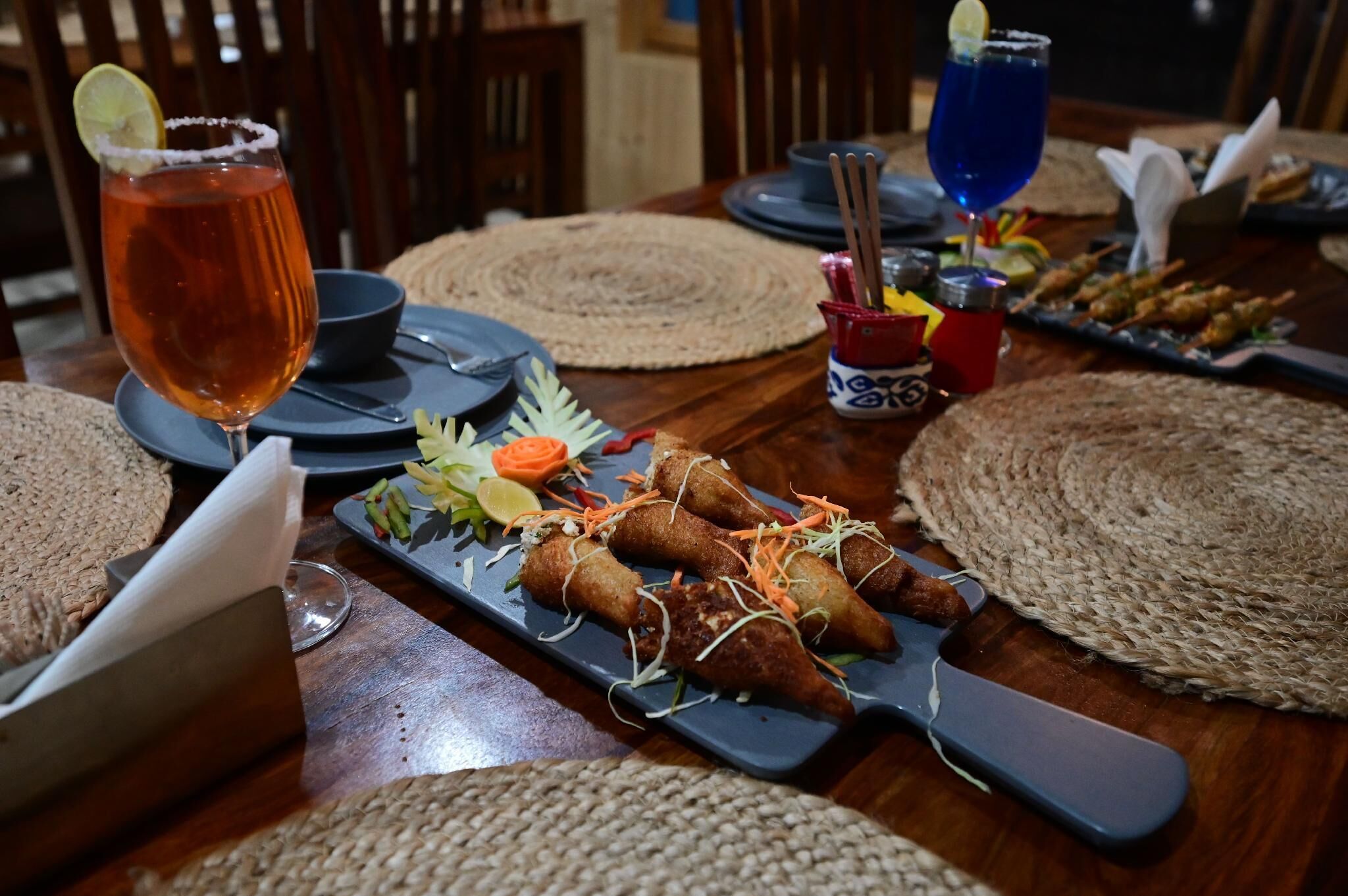 Une table à manger dressée avec une variété de plats, notamment des plats frits, et une boisson décorée d’une tranche de citron vert.