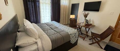 A hotel room with a bed, a desk, a chair, a TV, and curtains.