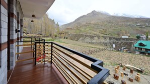 A balcony with a wooden floor and metal railing overlooking a mountainous landscape with a green-roofed building in the distance. - The Bulevar - Alpine (Lahul)