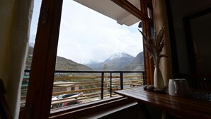A balcony with a view of snow-capped mountains, a wooden table with a vase and a teapot, and a railing. - The Bulevar - Alpine (Lahul)
