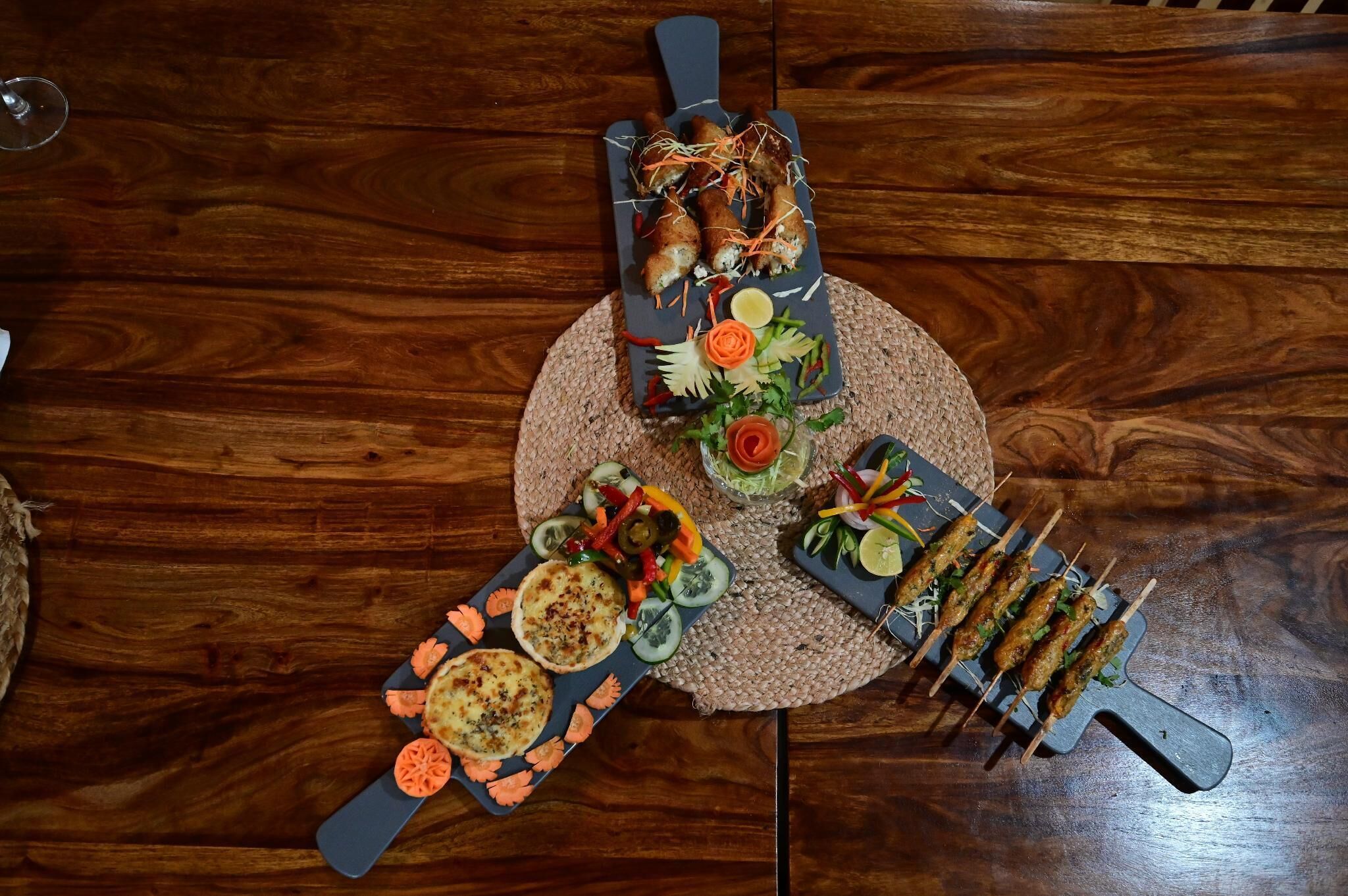 A wooden table with various food items arranged on a woven placemat.