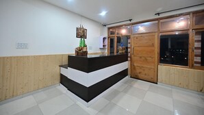 A reception area with a black and white counter, wooden paneling on the walls, and a large window with a view of the outside. - The Bulevar - Alpine (Lahul)