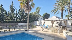 En pool med solstolar och ett avskärmat område med sittplatser.