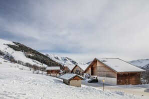 Un refugio de montaña cubierto de nieve con cabañas de madera, un aparcamiento y una vista despejada de las montañas circundantes.