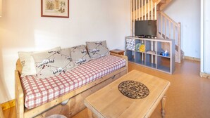 A cozy living room with a wooden sofa, a checkered table, and a TV on a shelf.