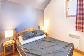 Ein Einzelbett mit hölzernem Kopfteil, zwei Nachttische mit Lampen, ein Fenster mit Vorhang und ein Wandheizkörper.
