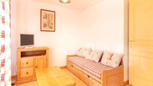 Une petite pièce agréable et chaleureuse, avec un lit en bois, une table en bois, un téléviseur posé sur un meuble en bois et un tableau encadré accroché au mur.