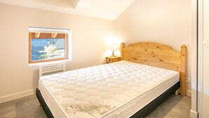 A bedroom with a wooden headboard, a window with a view, a bedside lamp, and a mattress.