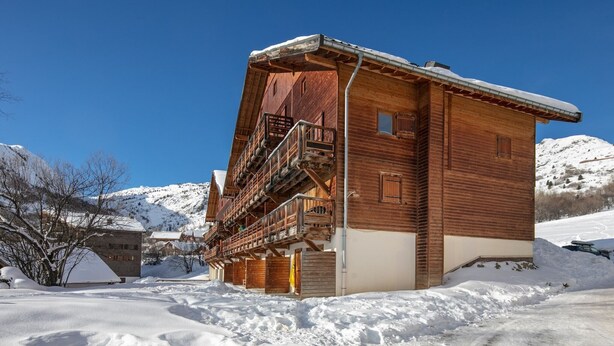 A wooden chalet with a balcony, surrounded by snow-covered mountains.