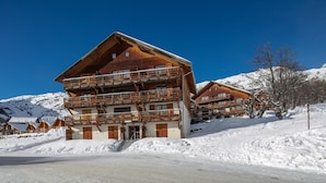 Eine mehrstöckige Holzhütte mit Balkonen vor verschneiter Bergkulisse.