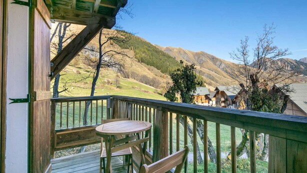 Een houten terras met een tafel en stoelen, met uitzicht op een bergachtig landschap met huizen.