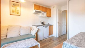 Een compacte woonruimte met een kitchenette, een bank, een kleine tafel en een deur naar een andere kamer.