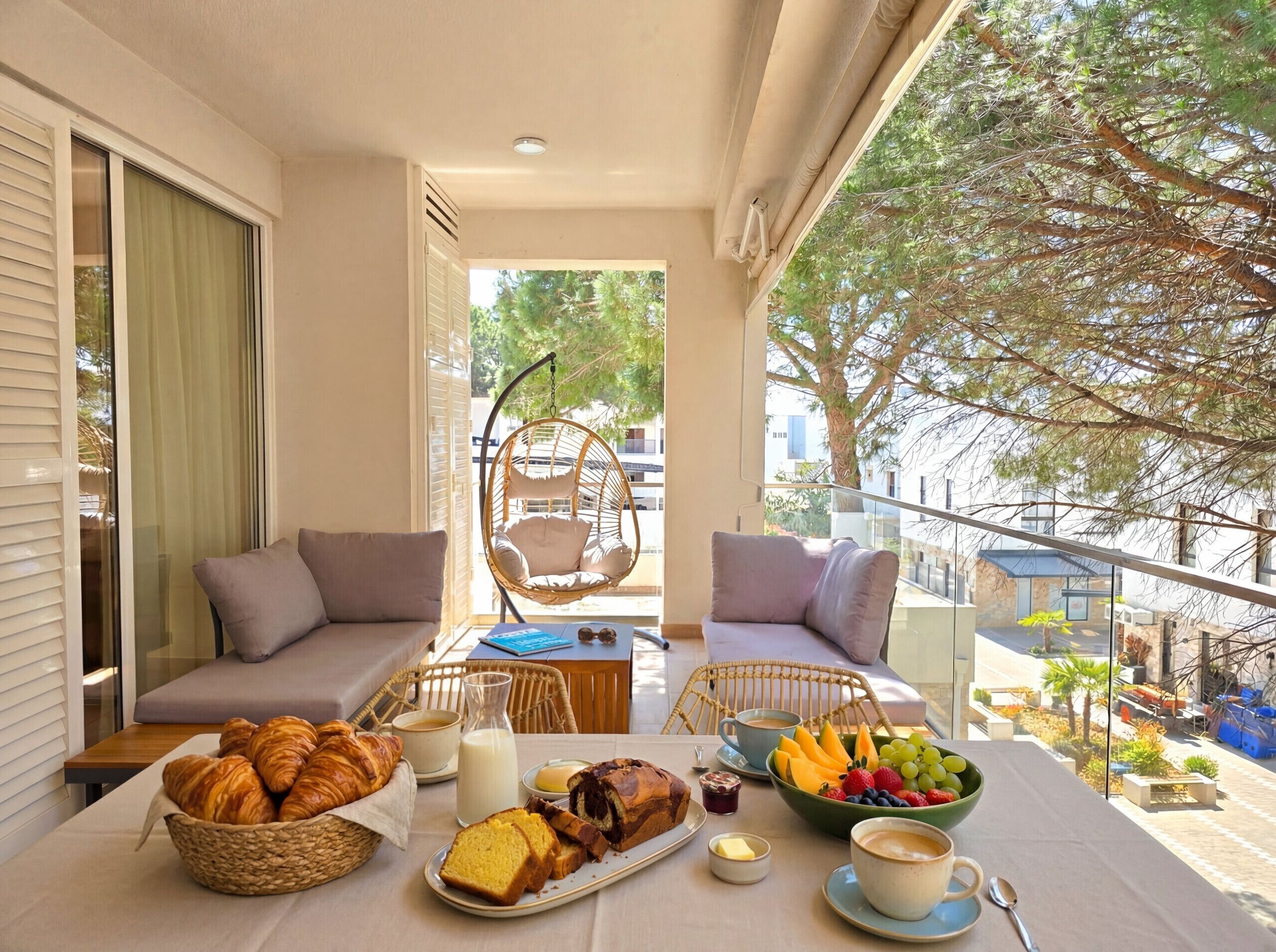 A balcony with a table set for breakfast, including croissants, bread, fruits, and beverages.