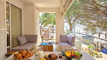 A balcony with a table set for breakfast, including croissants, bread, fruits, and beverages.