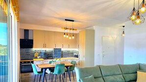 A modern kitchen with a dining area, a green sofa, and a view through the window.