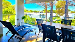 A balcony with a table and chairs, a potted plant, and a view of greenery and buildings.