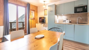A modern kitchen with a microwave, coffee maker, and sink. There is a dining table with chairs and a television in the corner. - Les Marmottes N°42 - 3P6 (Saint-Sorlin-d´Arves)