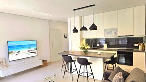 A modern kitchen with a central island, bar stools, a flat-screen TV, and a sofa. - SanPietro Holiday Homes 287 (Gjiri Lalzit)