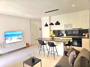 A modern kitchen with a central island, black bar stools, a flat-screen TV, and a sofa with a blanket.