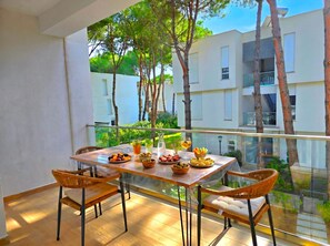 A balcony with a table set for breakfast, surrounded by wicker chairs, overlooking a residential area with trees and buildings.