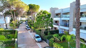 A residential street lined with parked cars and trees, leading to a multi-story building with balconies. - SanPietro Holiday Homes 287 (Gjiri Lalzit)