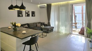 A modern living room with a sofa, a dining area with a marble table, and a balcony with curtains. - SanPietro Holiday Homes 287 (Gjiri Lalzit)