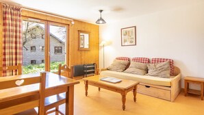 A cozy room with a wooden table, chairs, a sofa with checkered cushions, a lamp, and a window with curtains. - Les Grizzlis N°20 - 2P5 (Saint-Sorlin-d´Arves)
