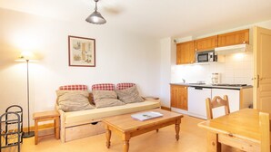 A compact living space with a sofa, a wooden table, a kitchen area with a microwave, and a ceiling light. - Les Grizzlis N°20 - 2P5 (Saint-Sorlin-d´Arves)