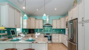 A modern kitchen with white cabinets, a central island with stools, a stainless steel refrigerator, and a teal backsplash. - Boca Grande Pool Home 343 - 4 bedroom / 4 Bath - Steps to Beach! (Boca Grande)
