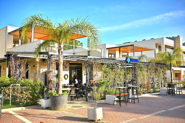 A restaurant with outdoor seating, palm trees, and a clear blue sky. - SanPietro Holiday Homes 294 (Gjiri Lalzit)