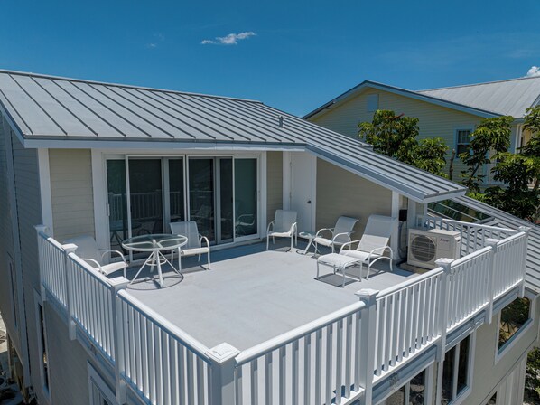A covered outdoor deck with white railings and seating, a sliding glass door, and an air conditioning unit.