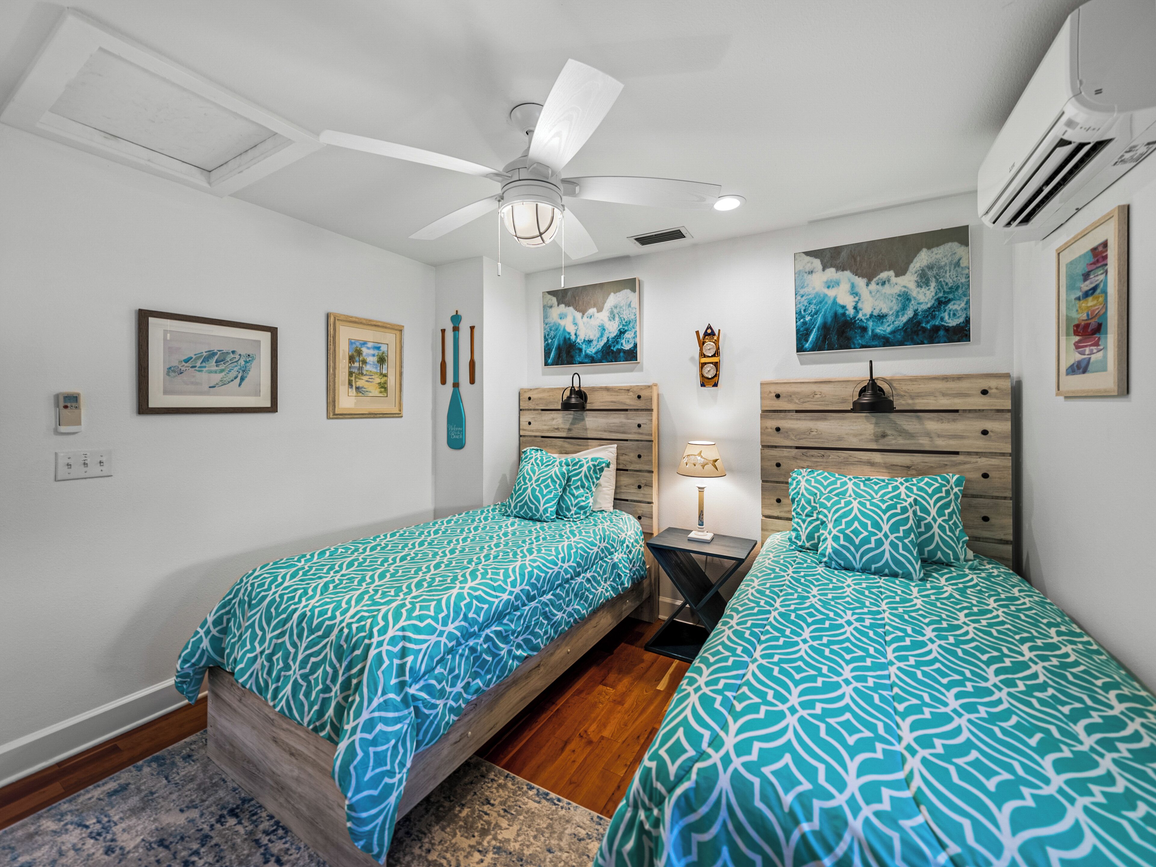 A bedroom with two beds, a ceiling fan, and artwork on the walls.