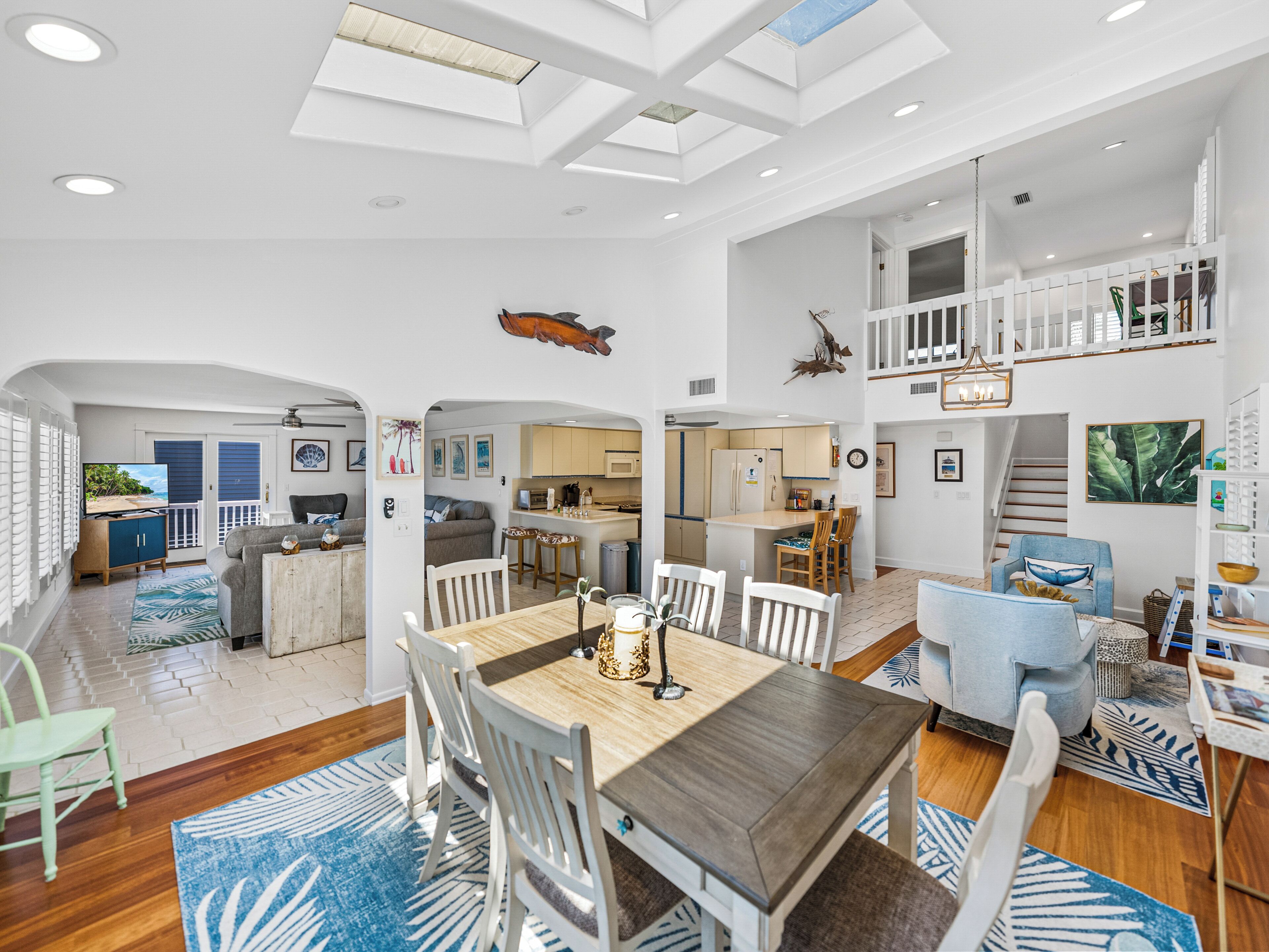 A spacious living area with a large wooden dining table, white chairs, and a kitchen in the background.