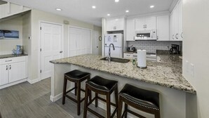 A modern kitchen with white cabinets, a granite countertop, a stainless steel sink, and two bar stools.